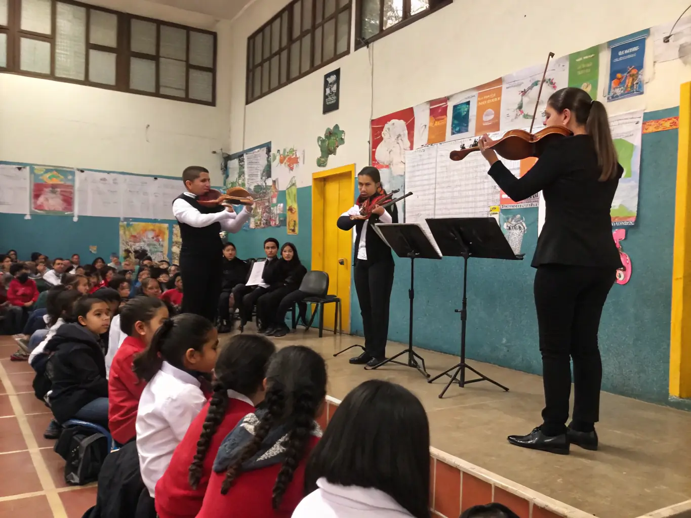 A photograph capturing a youth orchestra performing at a DISC HALL MUSIC event, showcasing young musicians collaborating and creating beautiful music together. The setting is a community hall, filled with an appreciative audience.